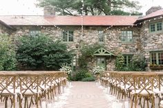 an outdoor ceremony set up with wooden chairs and flowers in front of a stone building