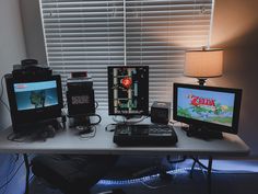 a desk with two monitors, a keyboard and a game controller on it next to a lamp