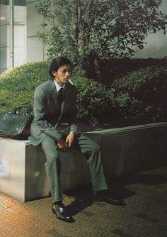 a man in a suit and tie sitting on a bench next to a planter