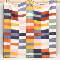 a multicolored quilt hanging on a wooden rail in front of a white wall