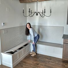 a woman standing next to a bench in a room with white walls and wood floors