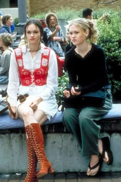 two young women sitting on a bench in front of a group of people, one wearing red and the other white