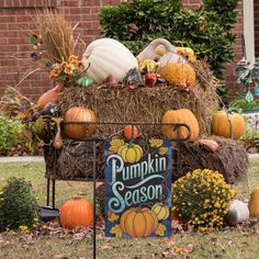 a pumpkin season sign surrounded by hay bales and fall decorations in front of a brick building