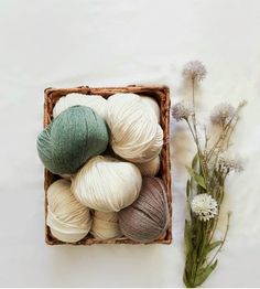 balls of yarn are in a basket next to a bouquet of wildflowers on a white surface