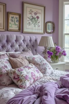 a bed with purple sheets and pillows in front of two framed pictures on the wall