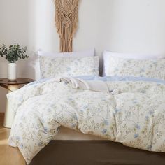 a bed with white and blue comforters in a room next to a plant on a table