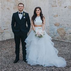 a bride and groom standing next to each other in front of an old stone wall