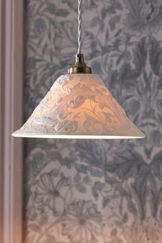 a white lamp hanging from a ceiling in front of a wallpapered room with floral designs