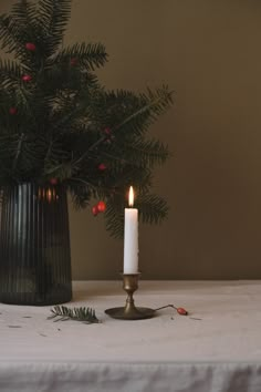 a lit candle sitting on top of a table next to a vase filled with christmas decorations