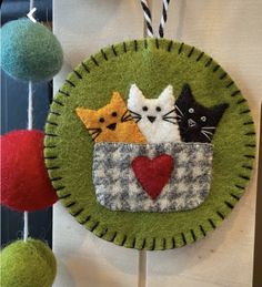 a green felt decoration with three cats in a basket and two balls hanging from the ceiling