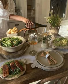 a woman pouring wine into a bowl on top of a table filled with plates and bowls