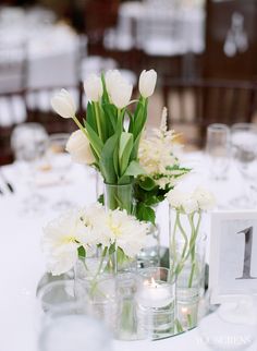 white flowers in vases on a table with candles and place cards for guests to sit at