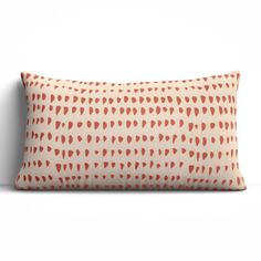 an orange and white pillow with red hearts on the front, against a white wall