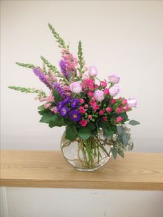 a vase filled with pink and purple flowers on top of a wooden table next to a white wall