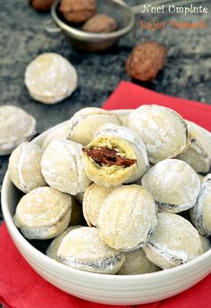 a white bowl filled with powdered sugar covered pastries on top of a red napkin