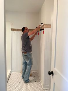 a man is working on the wall in his bathroom while holding up some screws