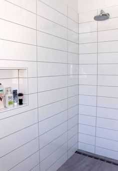 a white tiled shower with wooden flooring next to a wall mounted soap dispenser