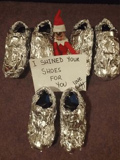 an elf is sitting on top of silver shoes with a sign that says i shinned your shoes for you