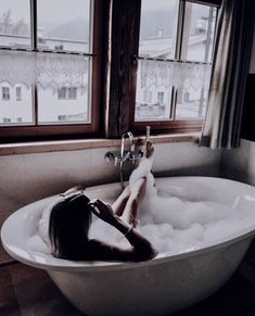 a woman sitting in a bathtub filled with foamy water next to a window