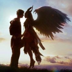 a man and woman standing next to each other in front of the sun with wings outstretched