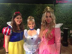 three women dressed up as disney characters posing for a photo in front of a hedge