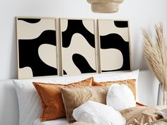 two black and white paintings on the wall above a bed with pillows, blankets and throw pillows