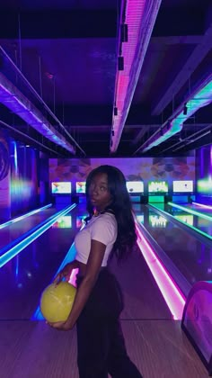 a woman holding a yellow ball in her right hand and bowling pins in the background