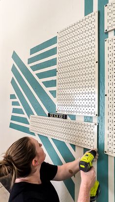 a woman is working on a wall with pegs and a drill bit in it