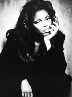 a black and white photo of a woman with her hand on her chin, leaning against a wall