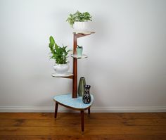 there is a plant stand with three potted plants on it and two vases in the corner