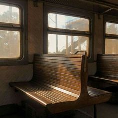 a wooden bench sitting next to two windows on a train car with sunlight streaming through the windows