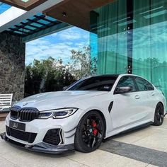 a white bmw car parked in front of a building with green glass walls and windows