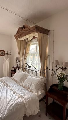 a bed with white sheets and pillows in a bedroom next to a wooden table topped with flowers