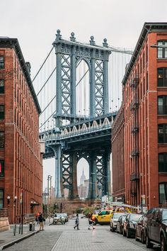 people walking on the sidewalk in front of some buildings and a large bridge above them