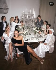 a group of women sitting around a table with white flowers and candles in the center