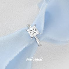 a white diamond ring sitting on top of a light blue satin ribbon with the word felicacas written below it