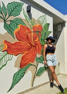 a woman standing in front of a flower painted on the side of a building with green leaves