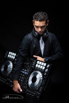 a man in a suit and tie holding two decks of dj equipment with headphones on his ears