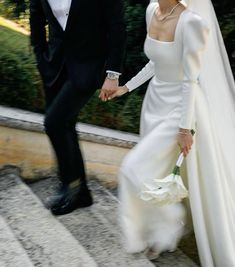 a bride and groom are walking down the stairs holding hands with each other while dressed in black tuxedos