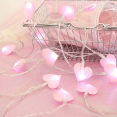 small pink hearts in a wire basket on a pink table cloth with string lights around it