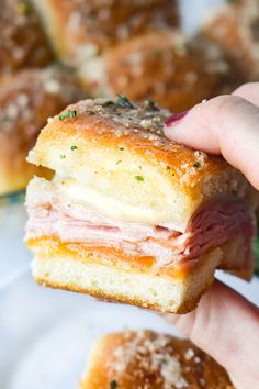 a hand holding a ham and cheese sandwich on a plate with other pastries in the background