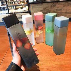 a person holding an item in front of four different colored containers on a wooden table