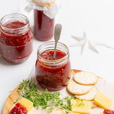 a plate with crackers, jam and cheese on it next to two jars of jelly