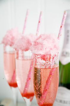 three champagne flutes filled with pink liquid and straws next to a bottle of booze