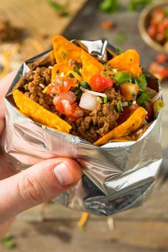 a hand holding up a foil container filled with taco meat and tortilla chips