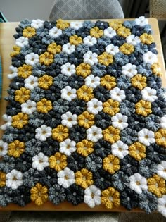 a crocheted blanket with yellow and white flowers on it sitting on top of a wooden table