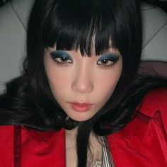 a woman with long black hair and blue eyes wearing a red jacket sitting in a car