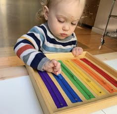 a toddler playing with an abacus in a wooden tray on the floor at home