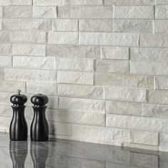 two black salt and pepper shakers sitting on top of a counter next to a white brick wall