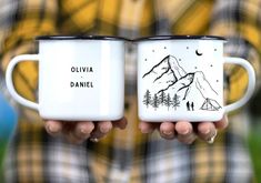 two people holding coffee mugs with mountains and trees painted on the sides, one in black and white